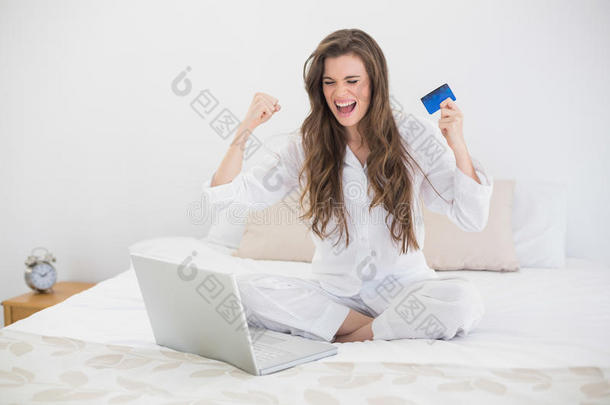 一位穿着白色睡衣的棕色头发的成功休闲女士用笔记本电脑在网上购物