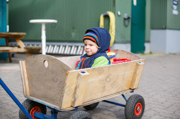 穿着秋装的木制手推车里的可爱的两岁小男孩
