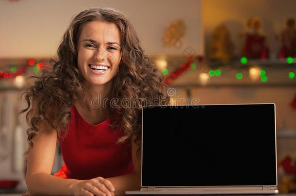 微笑的年轻<strong>主</strong>妇在厨房里展示笔记本<strong>电脑</strong>的空白<strong>屏幕</strong>