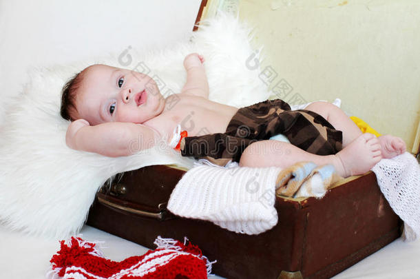 三个月大的快乐宝宝躺在带衣服的手提箱里