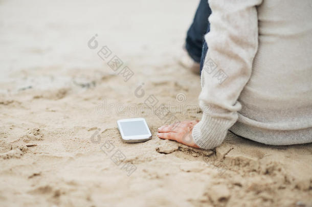 手机特写镜头靠近坐在沙滩上的女人