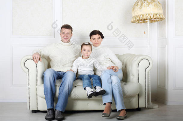 穿着白色毛衣和牛仔裤的幸福家庭坐在白色沙发上