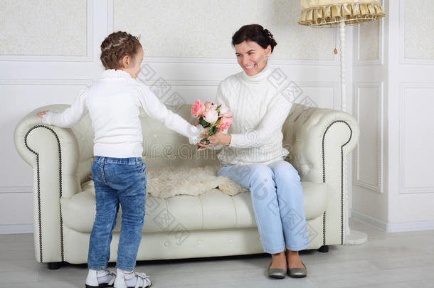 小女儿给坐在沙发上微笑的妈妈送花