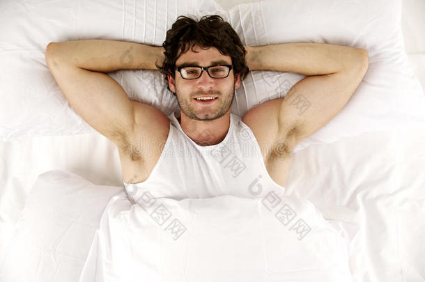 躺在白色床上的男人抬头看着镜头微笑着