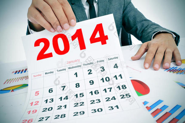 穿西装的男人拿着图表和2014年的日历