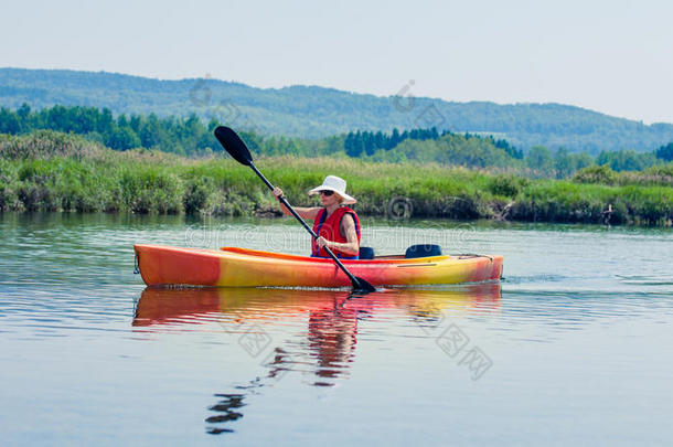 一个穿着安全背心的妇女独自在平静的河面上划独木舟