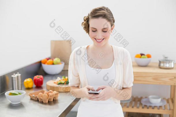 一位快乐的年轻女子站在厨房里用智能手机<strong>发信息</strong>