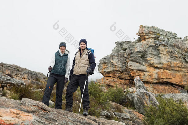 一对站在岩石上的夫妇，在晴朗的天空中用登山杖行走