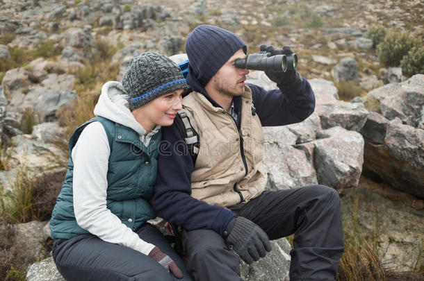 一对夫妇徒步旅行时用双筒望远镜坐在岩石上