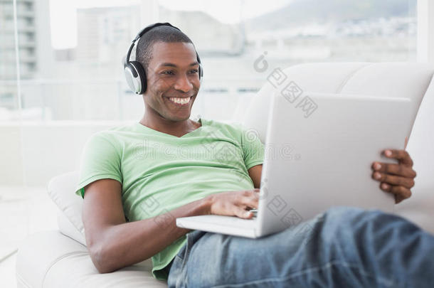 坐在沙发上用笔记本戴着耳机微笑的非洲男人