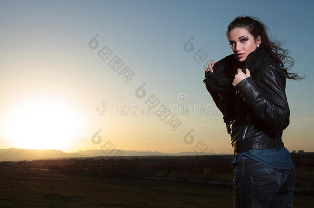 一个穿着皮夹克戴着围巾的女人，在黄昏中望着远方