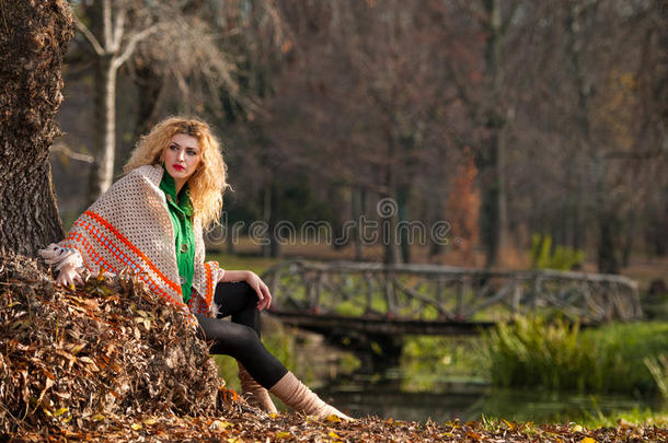 秋天的时候在公园里摆姿势的美女。穿着绿色上衣和大披肩的金发女孩在户外摆姿势。金色长发