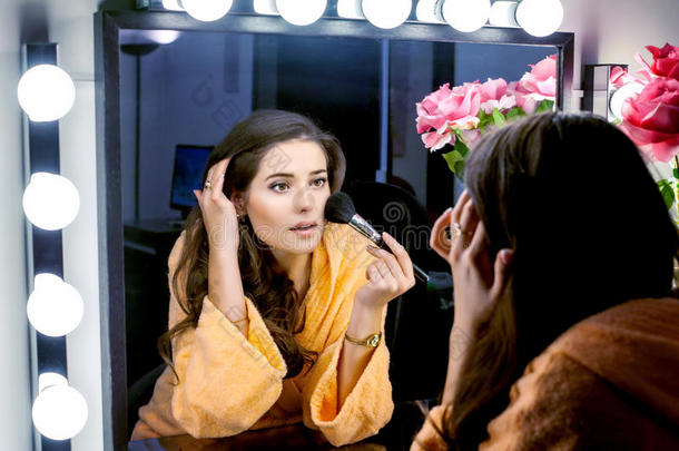 一个穿着<strong>橘色</strong>长袍的女人在镜子里化妆<strong>和</strong>打水