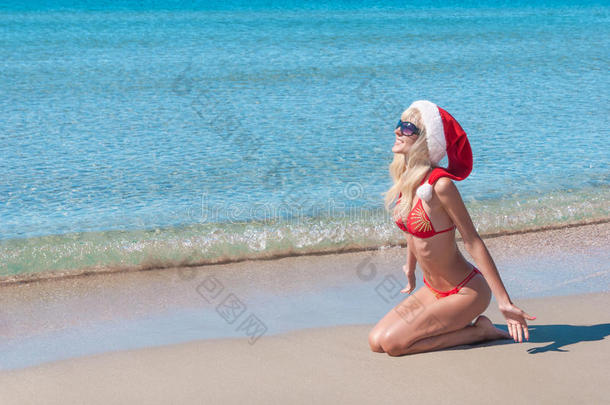 美丽的金发女人戴着红色圣诞帽和比基尼在海边