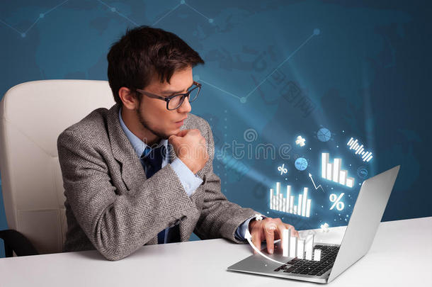 年轻人坐在办公桌旁，用笔记本电脑打字，上面有图表和