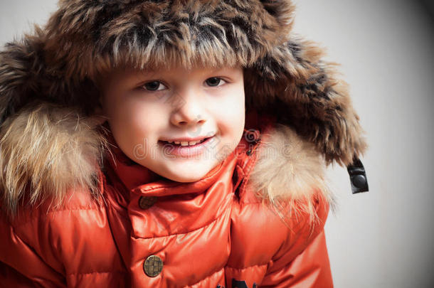 带着皮帽和橘色冬天的微笑的孩子夹克。时尚男孩