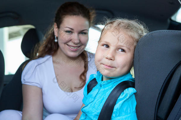 微笑的母亲带着女儿坐在汽车安全座椅上