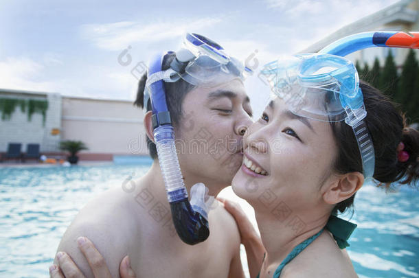 一对微笑的夫妇在游泳池里戴着<strong>潜水器</strong>亲吻脸颊