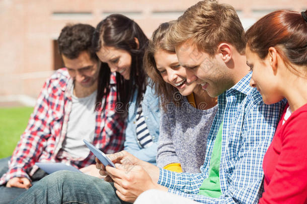 五个微笑的学生坐在草地上用平板电脑