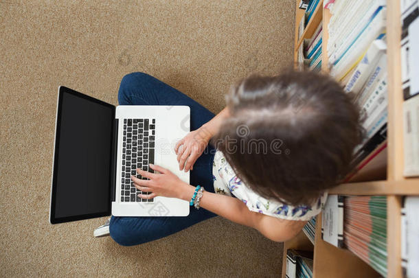 在<strong>图书馆</strong>地板上用笔记本电脑对着<strong>书架</strong>的学生