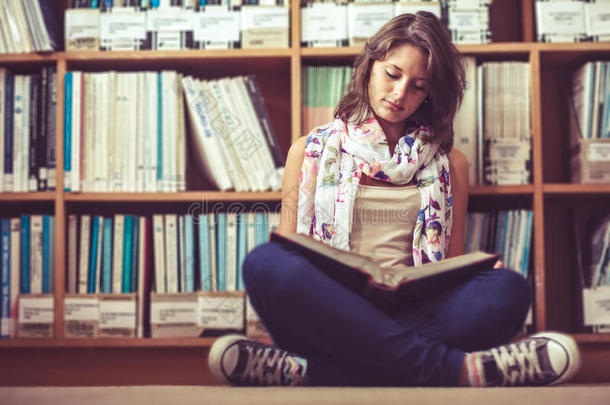 女学生靠着书架在图书馆地板上看书
