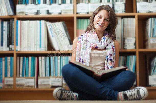 女学生对着书架微笑着在图书馆地板上看书