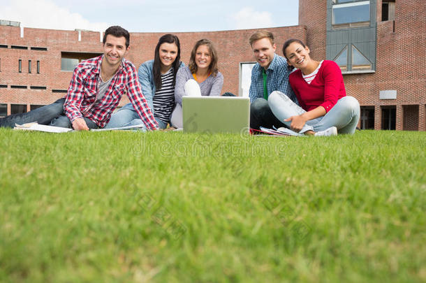 学生们拿着笔记本电脑在草坪上对着大学大楼