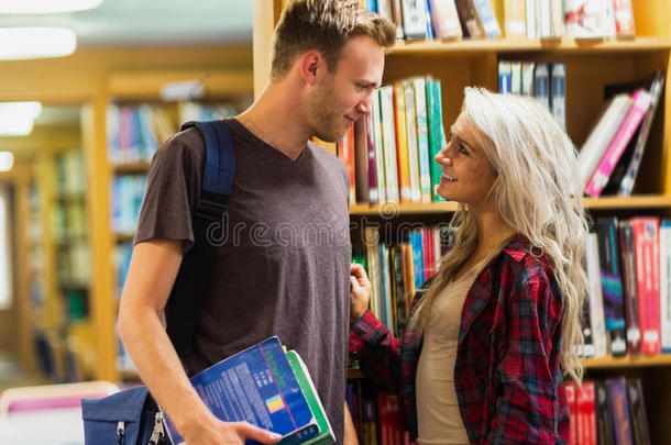 微笑的年轻夫妇靠在图书馆的书架上
