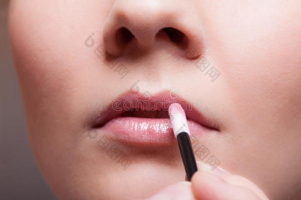 化妆。在唇部涂唇彩唇膏的女孩。脸的一部分。