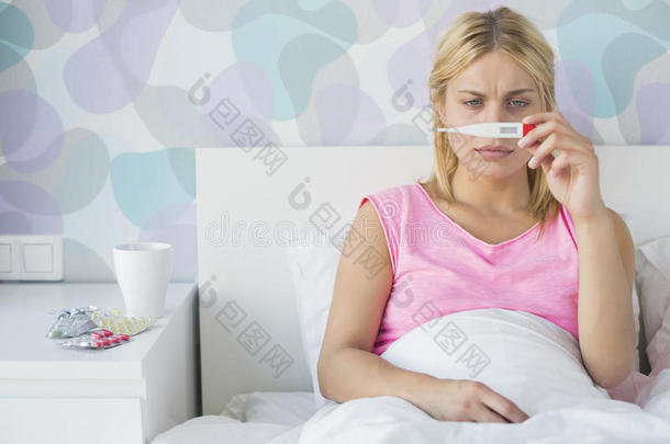 生病的年轻妇女在床上用<strong>体温</strong>计测<strong>体温</strong>