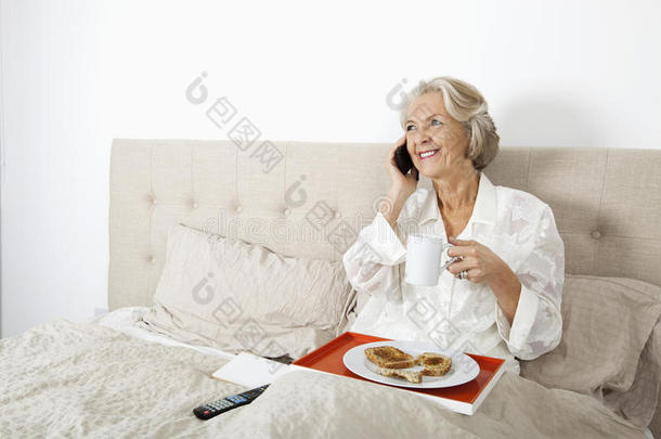 快乐的老太太在床上吃早餐时接听手机