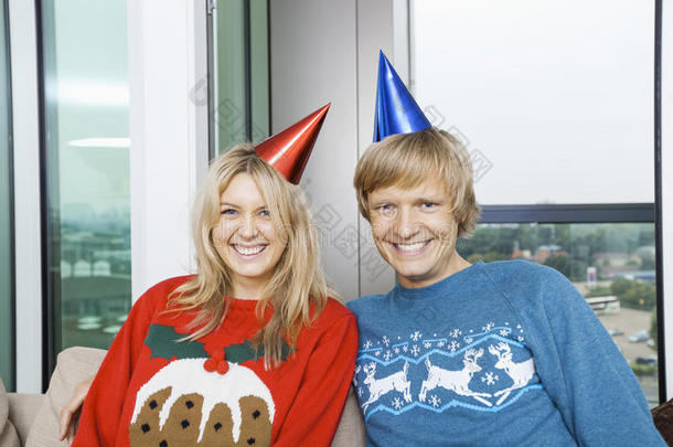 家里客厅里一对喜气洋洋的夫妇穿着圣诞毛衣戴着派对帽的画像