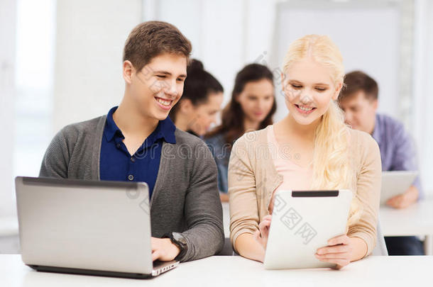 两个面带微笑的学生拿着笔记本电脑和平板电脑