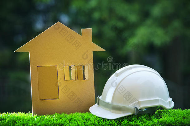 绿色草地上带安全帽的纸质家居线条，模糊复制空间背景，用于房地产和土地