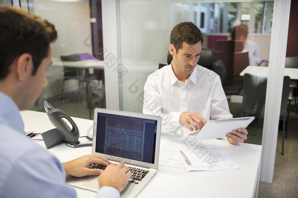 两个商人在办公室里用笔记本电脑和平板电脑工作