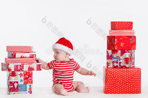 戴着圣诞帽的可爱的孩子坐在地板上，<strong>身边</strong>摆着成堆的礼物盒。白底隔离