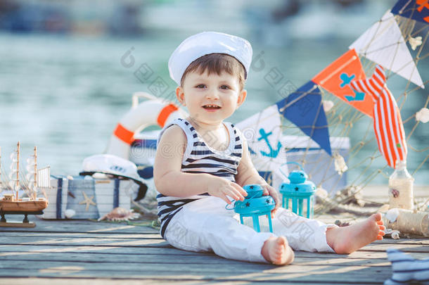 可爱的小男孩坐在户外码头的地板上，一种<strong>海洋风</strong>格。小水手