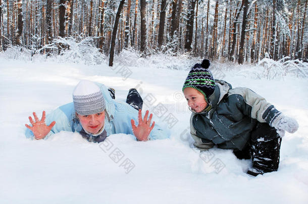 冬日的母亲带着儿子纵情地躺在森林里的雪地上