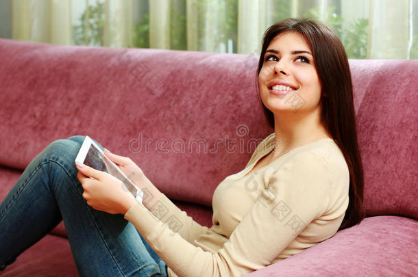 年轻快乐的女人拿着平板电脑躺在沙发上抬头看