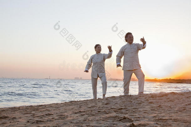 两位老人日落时在海滩上练习太极拳