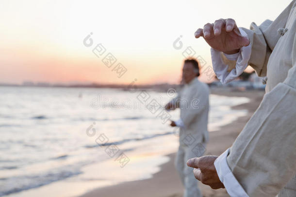 日落时分，两位老人在沙滩上练习太极拳，手拉近