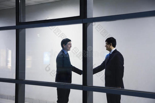 两个商人握手，透过玻璃墙看到