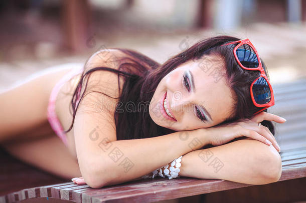 在热带旅游胜地，穿着比基尼日光浴的女士。美丽的年轻女子躺在游泳池附近的日光浴椅上。