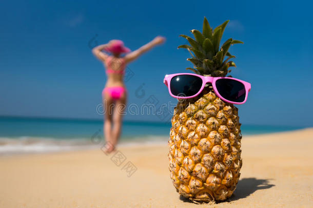一副欢快的菠萝眼镜和一个穿着比基尼的女人在海滩上晒日光浴。
