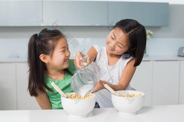 两个快乐的小女孩在厨房的碗里<strong>倒牛奶</strong>