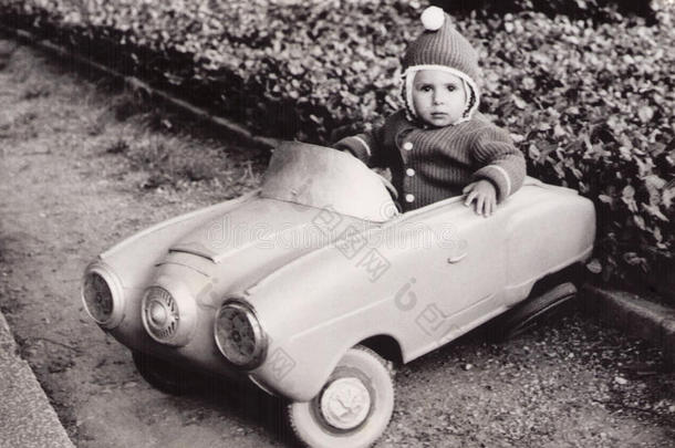 一个坐在玩具车里的小女孩的旧照片