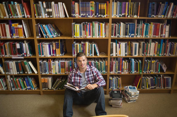 微笑的年轻学生坐在<strong>图书馆</strong>地板上<strong>看书</strong>