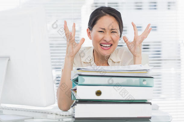 愤怒的女商人拿着一摞文件夹在办公桌上大叫