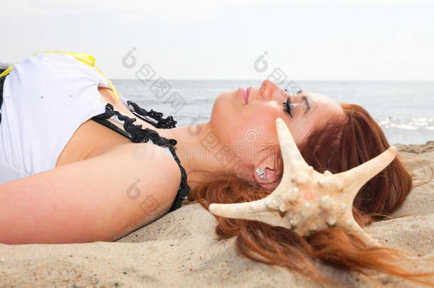 美丽的女孩躺在海边，带着贝壳自然度假