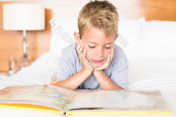 快乐的金发男孩躺在床上读故事书